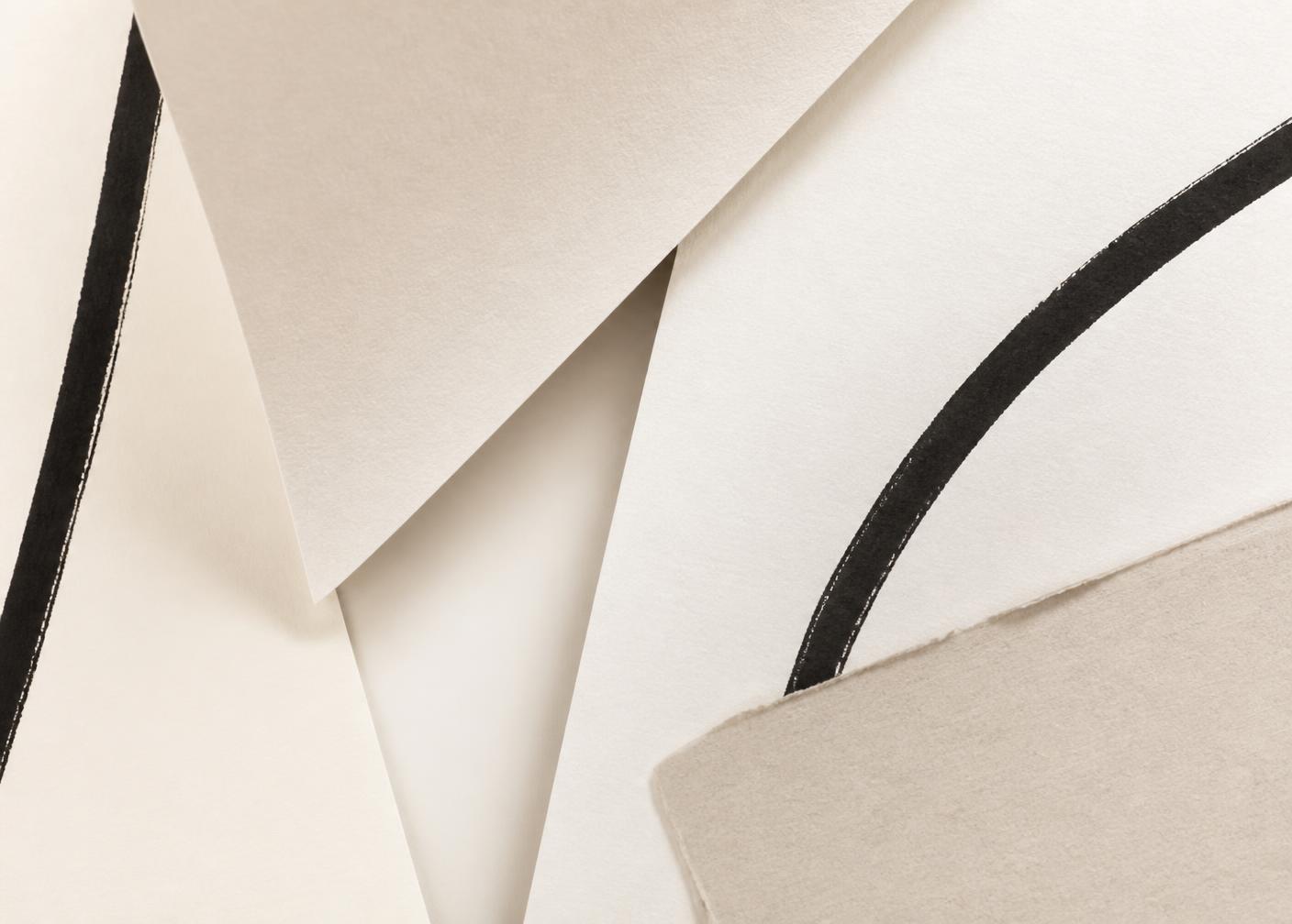 Close-up of overlapping ivory paper sheets with charcoal ink line accents